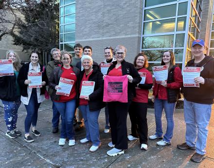 nurses stand in front of building holding "Stop the Cuts" and "Save Burdett Birth Center" signs