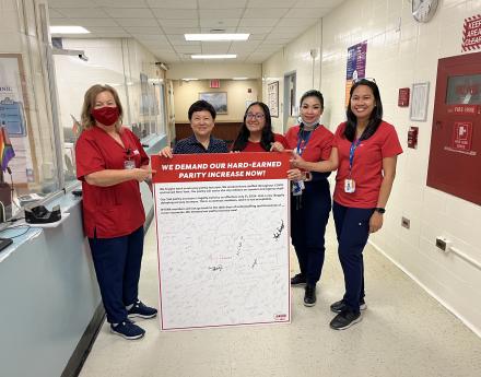 Elmhurst nurses hold a petition board demanding pay parity for NYC Health and Hospitals nurses